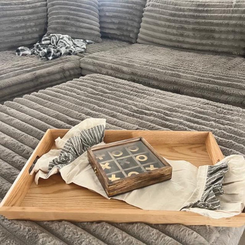 May include: A wooden tray with a gray and white patterned fabric and a wooden tic-tac-toe game with gold pieces.