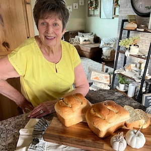 May include: Two loaves of freshly baked white bread on a wooden cutting board with a white cloth and white pumpkins.