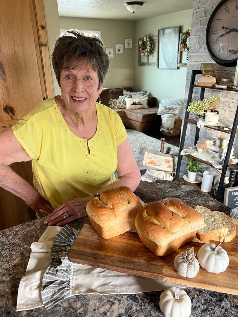 May include: Two loaves of freshly baked white bread on a wooden cutting board with a white cloth and white pumpkins.