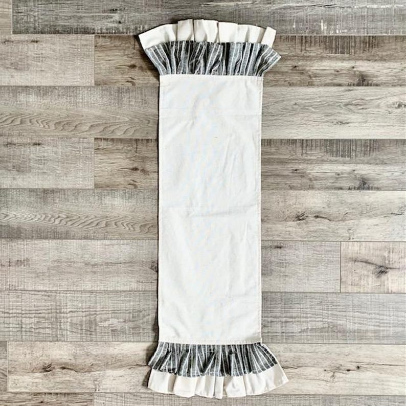 May include: White table runner with a black and white striped ruffle trim. The runner is made of a soft, lightweight fabric and is perfect for adding a touch of elegance to any table setting.