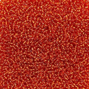May include: A close-up shot of a pile of small, orange seed beads. The beads have a metallic sheen, reflecting light. The beads are cylindrical and densely packed, creating a textured surface. Suitable for jewellery making and crafts.