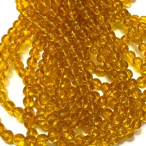 Peut inclure: Gros plan sur des brins de perles rondes, transparentes et jaune doré. Les perles sont enfilées ensemble, créant un effet texturé et superposé. Les perles sont de taille uniforme et semblent être en verre ou dans un matériau similaire. Le thème général est la fabrication de bijoux.