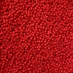 May include: A close-up shot of a mass of small, round, opaque red seed beads. The beads are uniform in size and closely packed together, forming a textured surface. Suitable for jewellery making and craft projects.