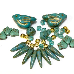 May include: A selection of turquoise and gold beads in diverse shapes, such as birds, shells, faceted rounds, and elongated teardrops. These beads are displayed on a white surface, suitable for jewellery making or craft projects.