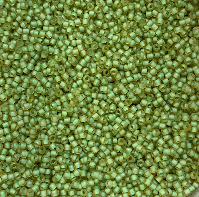 May include: Close-up of a pile of small, cylindrical beads in a pale green color. The beads are densely packed together, creating a textured surface. The beads appear to be made of a translucent material.