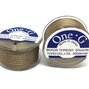 May include: Two spools of beige bead thread. Each spool has a clear plastic casing and a white and blue label with the text "One G BEADS THREAD 50 yards TOHO CO., LTD. 300 denier Made in Japan."