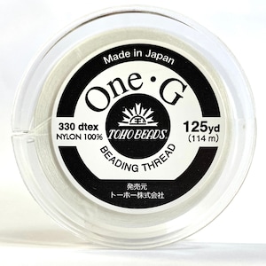 May include: A clear plastic spool containing clear nylon beading thread. The label, with black text on a white background, reads "One G" and "TOHO BEADS BEADING THREAD". It contains 114 m of thread, made in Japan.