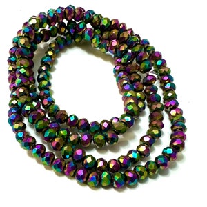 May include: Strands of iridescent faceted beads in shades of green, purple, and gold. The beads are strung together, creating a layered effect. The beads have a reflective, shimmering quality, and are set against a white background.