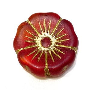 May include: A red flower-shaped bead with gold detailing. The bead features a gold sunburst design in the centre and gold accents around the edges. The bead is a deep red colour and has a matte finish.