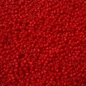 May include: A close-up of a mass of small, red, cylindrical beads. Each bead has a hole through the centre. The beads are scattered, creating a textured surface. The beads are a uniform size and shape.
