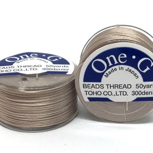 May include: Two spools of beige bead thread are shown against a white backdrop. Each spool has a clear plastic casing and a label with the text "One G BEADS THREAD 50yards TOHO CO.,LTD. 300denier Made in Japan."