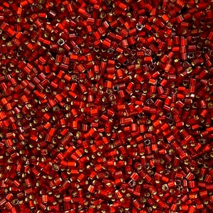 May include: A close-up shot of numerous small, cylindrical red beads. The beads are translucent, with a golden hue at the ends. They are tightly packed together, forming a textured surface. Suitable for jewellery making and various craft projects.