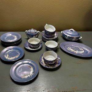 Op de afbeelding: Een vintage blauw en wit porseleinen theeservies met een drakenmotief. De set bevat kopjes, schotels, borden, een theepot, een afgedekte serveerschaal en een serveerschaal. Het drakenontwerp is goud en wit.