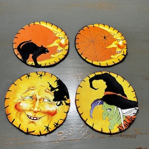 May include: Four round fabric coasters with a Halloween theme. Each coaster features a different design: a black cat, a spider web, a smiling moon face, and a witch with a green face.