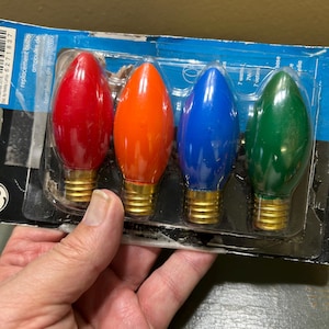 以下が含まれることがあります： 赤、オレンジ、青、緑の4つの交換用クリスマス電球のパッケージ。電球は涙の形をしており、金色のベースが付いています。パッケージには「replacement bulbs」の文字が含まれています。