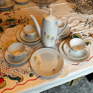 May include: A white tea set with a floral design. The set includes a teapot, four cups, and four saucers. The cups and saucers have a delicate floral pattern in shades of pink, yellow, and blue.