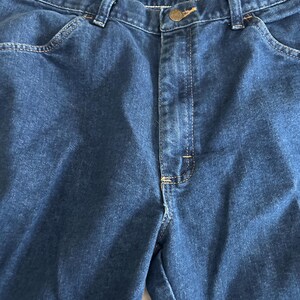 Pu&ograve; includere: Un paio di jeans in denim blu scuro con chiusura a bottone e cinque tasche.