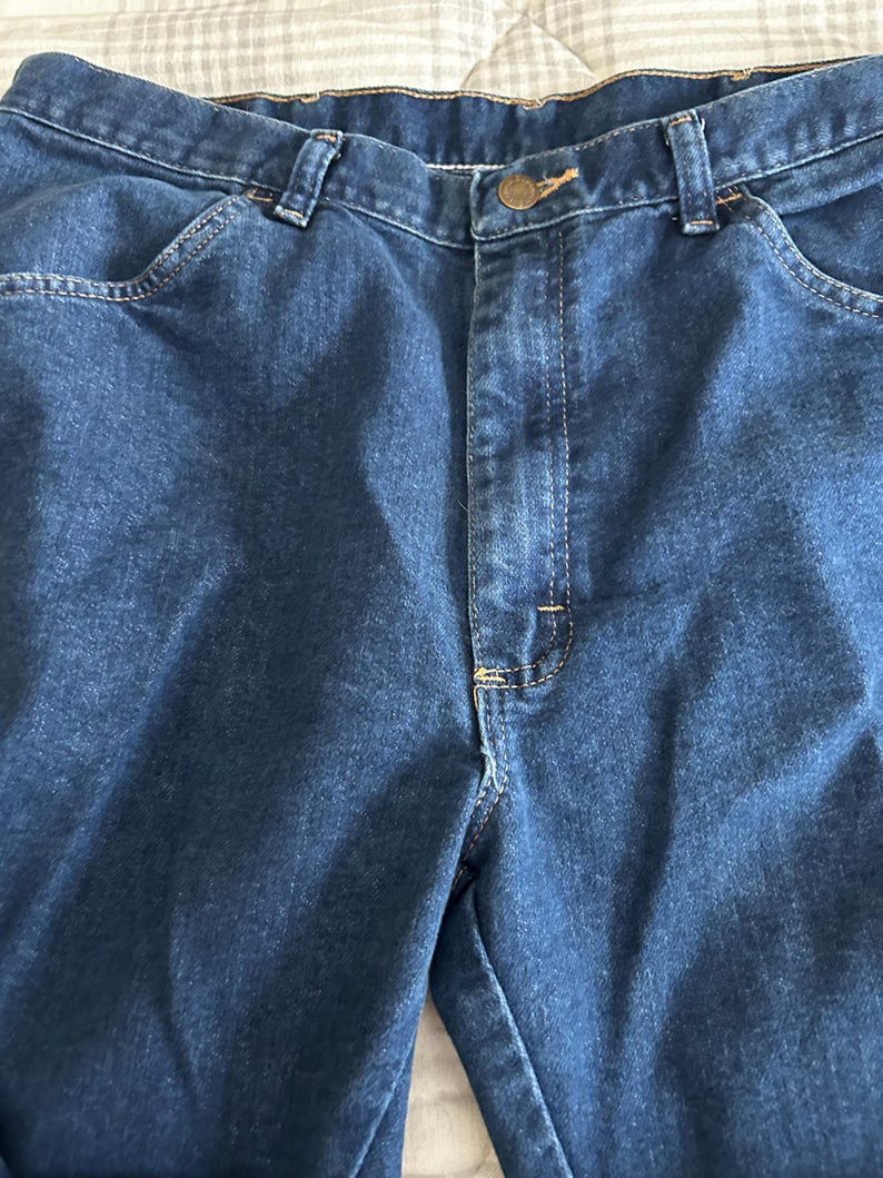 Pu&ograve; includere: Un paio di jeans in denim blu scuro con chiusura a bottone e cinque tasche.