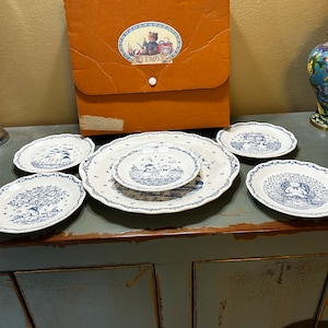 Puede incluir: Un juego de seis platos de porcelana azul y blanco con temática de osito de peluche. Los platos están dispuestos sobre una superficie de madera con una carpeta marrón etiquetada como "Teddy's" en el fondo.