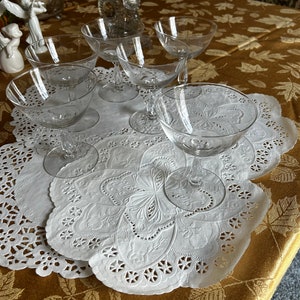 Könnte beinhalten: Fünf klare Glas-Stielgläser auf weißen Servietten auf einer goldenen Tischdecke mit Blatt-Muster.