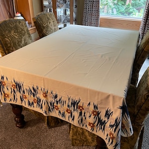 Könnte beinhalten: Eine beige Tischdecke mit einem schwarzen, blauen und braunen floralen Rand. Die Tischdecke liegt auf einem Holztisch mit vier Stühlen.