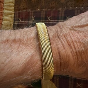 May include: A gold-toned metal expansion bracelet featuring a continuous, tightly coiled spring design. The band is constructed from numerous thin, parallel wire segments that allow the bracelet to stretch and fit securely around the wrist.