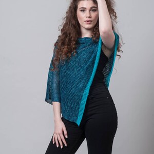 Puede incluir: Una mujer con el pelo largo y rizado casta&ntilde;o lleva un poncho de punto azul turquesa con un top negro de tirantes y unos vaqueros negros.