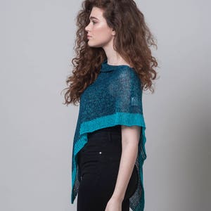 Puede incluir: Una mujer con un poncho de punto azul y negro, una camisa negra y pantalones vaqueros negros.