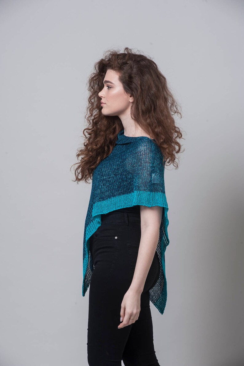 Puede incluir: Una mujer con un poncho de punto azul y negro, una camisa negra y pantalones vaqueros negros.