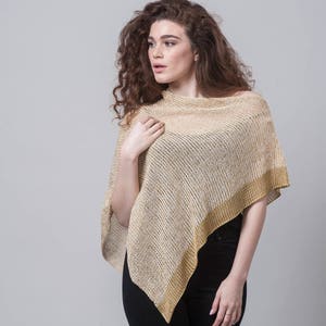 Puede incluir: Un poncho de punto beige y dorado con un corte holgado y una forma triangular. El poncho está hecho de una tela ligera y tiene un brillo sutil.