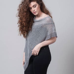 Puede incluir: Una mujer con un poncho de punto gris de corte holgado y pantalones vaqueros negros.