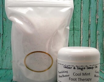 May include: A white plastic bag filled with a white foot scrub and a white jar of foot cream. The jar has a black label with the text "Cedar & Sage Soap Co. Cool Mint Foot Therapy 4 oz. Nourishing Shea Butter Cool Menthol".
