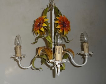 May include: A white metal chandelier with three candle-style lights. The chandelier is decorated with orange and yellow flower accents and green leaves. The light bulbs are clear and the fixture has a vintage look.