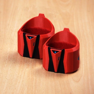 Può includere: Due porta bicchieri stampati in 3D di colore rosso e nero con una luce blu al centro di ciascuno. I porta bicchieri sono progettati per contenere un bicchiere di dimensioni standard.