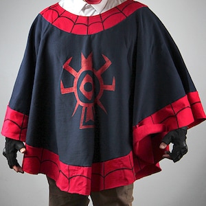 Puede incluir: Una capucha de poncho azul oscuro con un diseño de telaraña roja y un símbolo rojo en la parte delantera. La capucha tiene un borde rojo alrededor de los bordes.