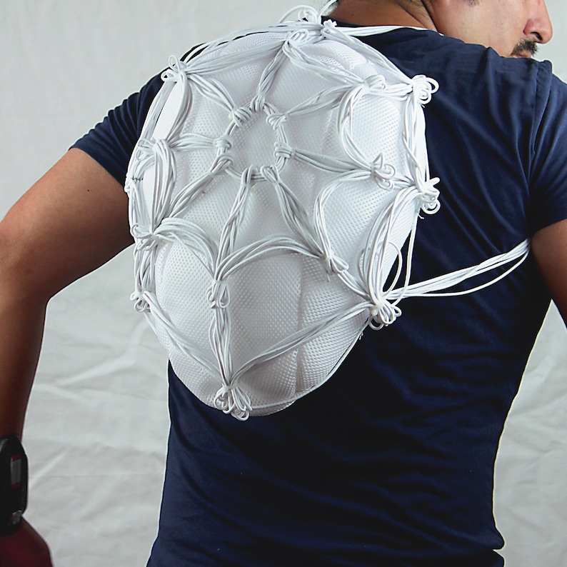 May include: A white, web-like structure made of string is worn on the back of a person. The structure is attached to straps that go over the shoulders.