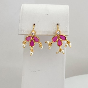 May include: A pair of gold-colored earrings with a floral design. Each earring features three fuchsia-colored petals, a clear gemstone, and small white pearls. The earrings are displayed on a white stand.