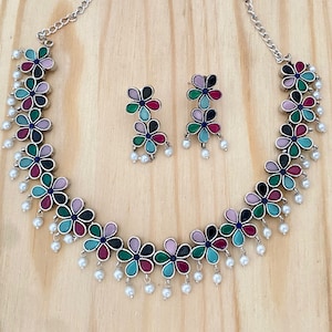 Op de afbeelding: Een zilveren ketting met een bloemmotief met gekleurde stenen en parel accenten. Passende oorbellen met hetzelfde bloemmotief zijn inbegrepen.