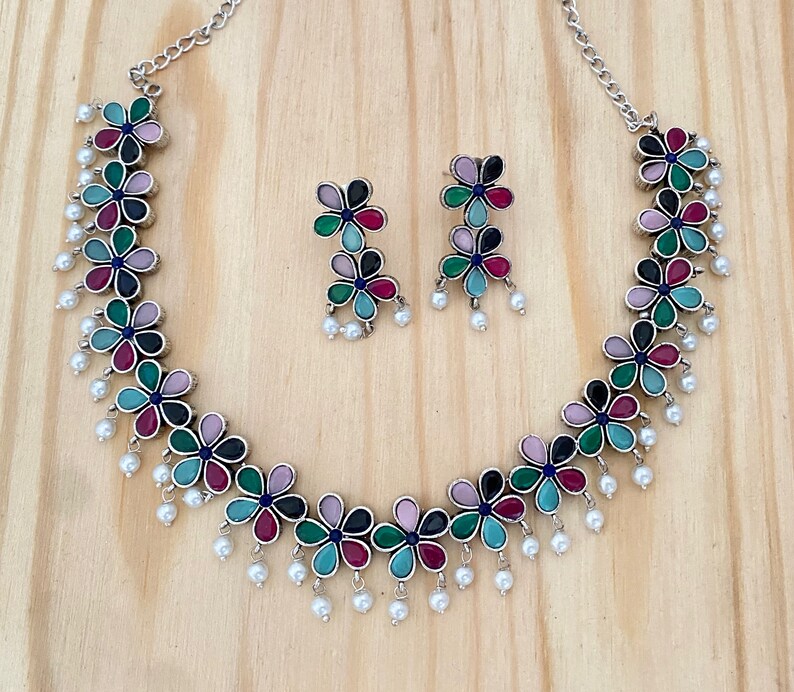 Op de afbeelding: Een zilveren ketting met een bloemmotief met gekleurde stenen en parel accenten. Passende oorbellen met hetzelfde bloemmotief zijn inbegrepen.