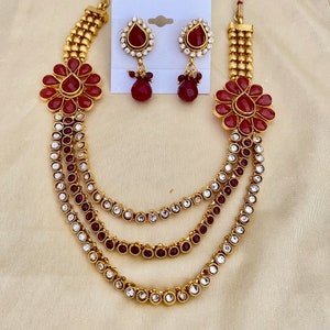 Puede incluir: Un collar de oro con cuatro hileras de piedras rojas y transparentes, dos colgantes de flores rojas a juego y un par de pendientes de piedras rojas y transparentes.