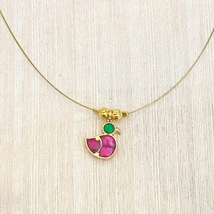 May include: A gold chain necklace with a small bird pendant. The bird is made of gold and has a pink and green gemstone inlay.