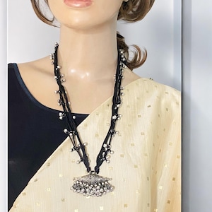 May include: A black necklace with silver beads and a large silver pendant. The pendant is shaped like a dome with a fringe of silver beads.