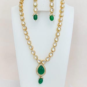 May include: A gold necklace and earrings set with a green stone pendant and matching earrings. The necklace is made of small, teardrop-shaped stones.