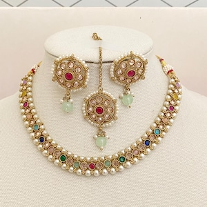 May include: A gold necklace with white pearls and colorful stones, a matching pair of earrings, and a gold pendant with a pink stone.