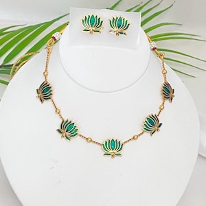 May include: A gold-toned necklace and matching earrings set. The necklace features green lotus flower pendants connected by small gold beads. The earrings have a matching lotus flower design. The jewelry is displayed on a white bust.