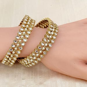 May include: Two gold bangles with white pearlescent stones and small white beads.