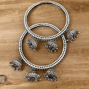 May include: Two silver bangles with dangling bells. The bangles are decorated with a repeating pattern of small circles.