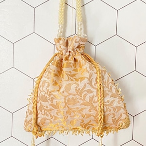 May include: A small, gold and white drawstring bag with a pearl handle. The bag has a floral pattern and a fringed trim.