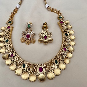 May include: A gold necklace with a coin design and pink and green gemstones. Matching earrings with pink and green gemstones.