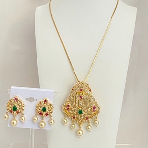 May include: A gold necklace with a pendant featuring a detailed design with white, red, and green stones. The pendant is attached to a delicate chain and has pearl drops. Matching earrings with the same design and pearl drops are included.